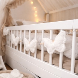 Girlanda z miękkimi motylkami teddy w kolorze beżowym zawieszona na łóżeczku dziecięcym w przytulnym pokoju niemowlęcym