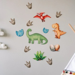 Kolorowe naklejki ścienne z dinozaurami, jajkami i tropami na jasnej ścianie w pokoju dziecka.