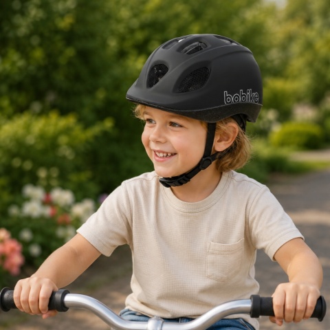 Dziecko jadące na rowerze w czarnym kasku dziecięcym Bobike GO podczas aktywności na świeżym powietrzu