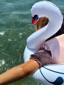 Dziecko w dmuchanym kole do pływania łabędź Vanilla Copenhagen podczas zabawy w wodzie na plaży