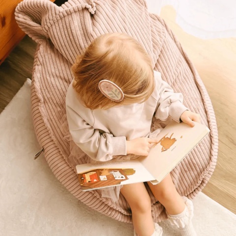 Dziewczynka czytająca książkę na różowej pufie Teddy Aesthetic – widok z góry