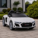 Białe Audi R8 na akumulator dla dziecka ustawione na tarasie przed nowoczesnym domem – licencjonowany samochód elektryczny