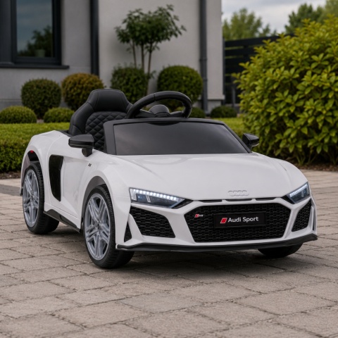 Białe Audi R8 na akumulator dla dziecka ustawione na tarasie przed nowoczesnym domem – licencjonowany samochód elektryczny