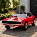 Czerwony Dodge Charger R/T na akumulator dla dzieci w aranżacji ogrodu przy nowoczesnym domu.