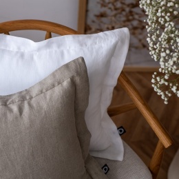 Poduszka lniana z rantem Linen Natural w naturalnym beżowo-szarym kolorze na drewnianym fotelu