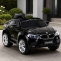 Czarne BMW X6M na akumulator dla dzieci przed nowoczesnym domem