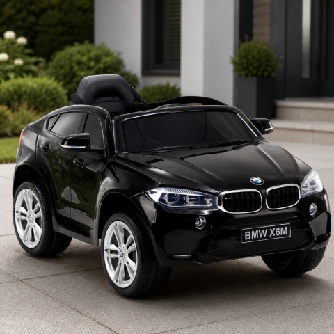Czarne BMW X6M na akumulator dla dzieci przed nowoczesnym domem