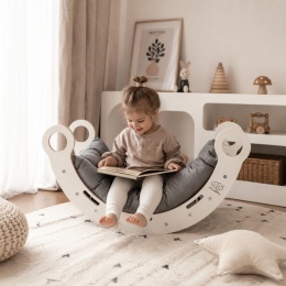 Dziecko siedzące na drewnianym bujaku Montessori MeowBaby z szarą poduszką w przytulnym pokoju dziecięcym