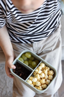 Dziecko trzyma zielony silikonowy lunchbox z trzema przegrodami