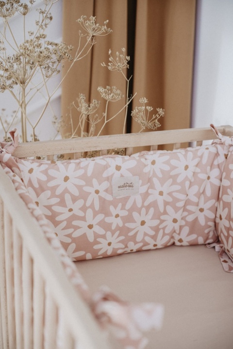 Różowy ochraniacz do łóżeczka Malomi Blush Daisies w białe stokrotki, zawiązany na drewnianym łóżeczku dziecięcym.