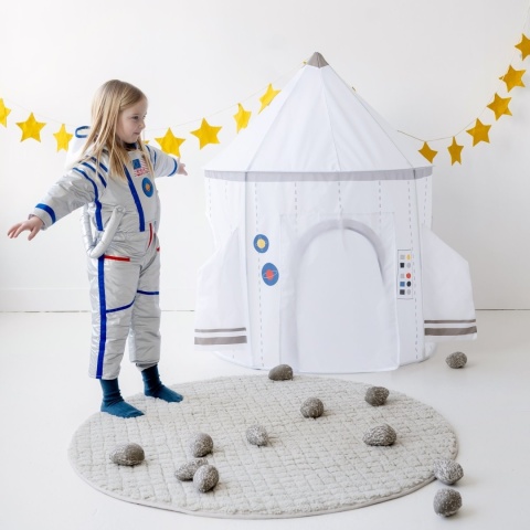 Dziewczynka w stroju astronautki bawi się obok namiotu rakiety kosmicznej w pokoju dziecięcym