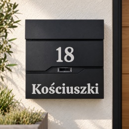 Czarna skrzynka na listy z numerem domu 18 i napisem Kościuszki, zamontowana na jasnej elewacji